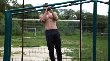 Genç kaslı sporcu spor alanında barfiks çekiyor. Atletik adam dışarıda egzersiz yapıyor. Yaz doğasında spor yapan güçlü bir adam. Sağlıklı ve aktif yaşam tarzı kavramı. Yavaş çekim