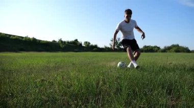 Üniformalı profesyonel futbolcu yeşil sahada koşarken topa numara yapıyor. Sporcu güneşli bir günde Meadow 'da koşarken topa vurur. Stadyumda antrenman yapan genç adam. Serbest stil futbol.