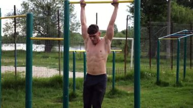 Atletik adam karın kaslarını eğitir spor sahasında yatay barda bacak kaldırır. Genç sporcu, barfiks çekme çubuğunda egzersiz yapıyor. Doğada spor yapan sporcu. Sağlıklı yaşam tarzı.