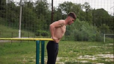 Genç sporcu doğada paralel barlarda şınav çekiyor. Spor alanında egzersiz yapan güçlü bir sporcu. Erkek üstsüz sporcu dışarıda sıkı çalışıyor. Aktif spor yaşam tarzı kavramı. Yavaş