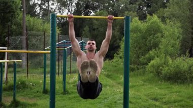Atletik adam karın kaslarını eğitir spor sahasında yatay barda bacak kaldırır. Genç sporcu, barfiks çekme çubuğunda egzersiz yapıyor. Doğada spor yapan sporcu. Sağlıklı yaşam tarzı.