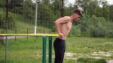 Genç sporcu doğada paralel barlarda şınav çekiyor. Spor alanında egzersiz yapan güçlü bir sporcu. Erkek üstsüz sporcu dışarıda sıkı çalışıyor. Aktif spor yaşam tarzı kavramı. Yavaş çekim
