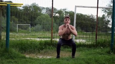 Spor sahasında çömelme hareketleri yapan erkek üstsüz atlet. Yaz doğasında çalışan genç bir sporcu. Güçlü sporcu dışarıda egzersiz yapıyor. Aktif ve sportif yaşam tarzı kavramı. Yavaş çekim