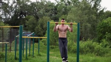 Güçlü ve kaslı bir adam doğanın yatay çubuğunda egzersiz yapıyor. Spor sahasında sıkı gömleksiz sporcu. Genç atletik adam dışarıda egzersiz yapıyor. Sağlıklı yaşam tarzı kavramı.
