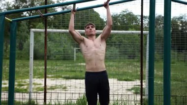 Genç kaslı sporcu spor alanında barfiks çekiyor. Atletik adam dışarıda egzersiz yapıyor. Yaz doğasında spor yapan güçlü bir adam. Sağlıklı ve aktif yaşam tarzı kavramı. Yavaş çekim