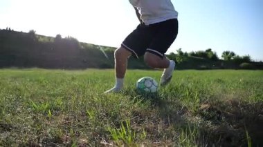 Profesyonel futbolcunun erkek ayağı, yeşil sahada koşarken topla numaralar gösterir. Güneşli bir günde Meadow 'da koşan sporcu bacakları topa vurur. Stadyumda antrenman yapan genç adam. Yavaş çekim