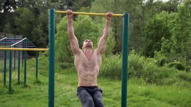 Atletik adam karın kaslarını eğitir spor sahasında yatay barda bacak kaldırır. Genç sporcu, barfiks çekme çubuğunda egzersiz yapıyor. Doğada spor yapan sporcu. Sağlıklı yaşam tarzı.