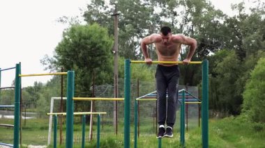 Cesur üstsüz sporcu doğada yatay çıtada şınav çekiyor. Güçlü ve kaslı adam spor alanında antrenman yapıyor. Genç atletik adam dışarıda egzersiz yapıyor. Aktif ve sağlıklı yaşam tarzı kavramı.