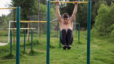 Spor sahasında karın kaslarını çalıştıran güçlü bir adam. Genç sporcu, barfiks çekme çubuğunda egzersiz yapıyor. Doğada spor yapan sporcu. Sportif yaşam tarzı kavramı.