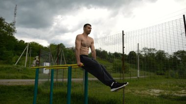 Güçlü bir adam karın kaslarını eğitir spor sahasında paralel barlarda bacak kaldırır. Genç üstsüz sporcu doğada egzersiz yapıyor. Doğada spor yapan sporcu. Sportif yaşam tarzı kavramı.