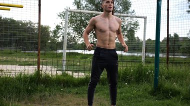 Spor sahasında çömelme hareketleri yapan erkek üstsüz atlet. Yaz doğasında çalışan genç bir sporcu. Güçlü sporcu dışarıda egzersiz yapıyor. Aktif ve sportif yaşam tarzı kavramı. Yavaş çekim