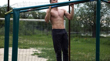 Genç kaslı sporcu spor alanında barfiks çekiyor. Atletik adam dışarıda egzersiz yapıyor. Yaz doğasında spor yapan güçlü bir adam. Sağlıklı ve aktif yaşam tarzı kavramı. Yavaş çekim