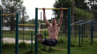 Atletik adam karın kaslarını eğitir spor sahasında yatay barda bacak kaldırır. Genç sporcu, barfiks çekme çubuğunda egzersiz yapıyor. Doğada spor yapan sporcu. Sağlıklı yaşam tarzı.