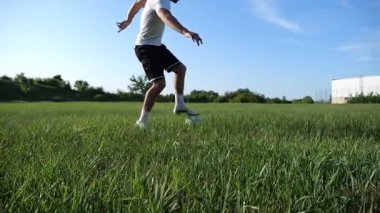 Üniformalı profesyonel futbolcu yeşil sahada koşarken topa numara yapıyor. Sporcu güneşli bir günde Meadow 'da koşarken topa vurur. Stadyumda antrenman yapan genç adam. Serbest stil futbol.