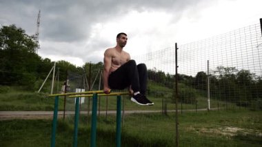 Spor alanında paralel barlarda karın kaslarını çalıştıran güçlü bir adam. Genç üstsüz sporcu doğada egzersiz yapıyor. Doğada spor yapan sporcu. Aktif spor yaşam tarzı kavramı.