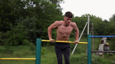 Cesur üstsüz sporcu doğada yatay çıtada şınav çekiyor. Güçlü ve kaslı adam spor alanında antrenman yapıyor. Genç atletik adam dışarıda egzersiz yapıyor. Aktif ve sağlıklı yaşam tarzı kavramı.