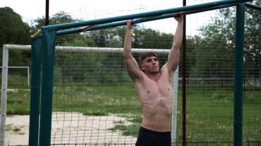 Genç kaslı sporcu spor alanında barfiks çekiyor. Atletik adam dışarıda egzersiz yapıyor. Yaz doğasında spor yapan güçlü bir adam. Sağlıklı ve aktif yaşam tarzı kavramı. Yavaş çekim