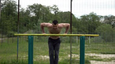 Cesur üstsüz sporcu doğadaki paralel parmaklıklar üzerinde egzersiz yapıyor. Spor alanında çalışan güçlü ve kaslı bir adam. Genç atletik adam dışarıda egzersiz yapıyor. Aktif sağlıklı yaşam tarzı kavramı.