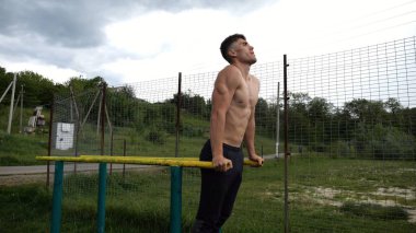Genç sporcu doğada paralel barlarda şınav çekiyor. Spor alanında egzersiz yapan güçlü bir sporcu. Erkek üstsüz sporcu dışarıda sıkı çalışıyor. Aktif spor yaşam tarzı kavramı. Yavaş çekim