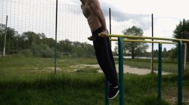 Genç sporcu doğada paralel barlarda şınav çekiyor. Spor alanında egzersiz yapan güçlü bir sporcu. Erkek üstsüz sporcu dışarıda sıkı çalışıyor. Aktif spor yaşam tarzı kavramı. Yavaş çekim