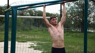 Genç kaslı sporcu spor alanında barfiks çekiyor. Atletik adam dışarıda egzersiz yapıyor. Yaz doğasında spor yapan güçlü bir adam. Sağlıklı ve aktif yaşam tarzı kavramı. Yavaş çekim