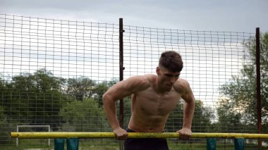 Erkek üstsüz sporcu doğada paralel barlarda şınav çekiyor. Spor alanında egzersiz yapan güçlü bir sporcu. Genç sporcu dışarıda sıkı çalışıyor. Aktif spor yaşam tarzı kavramı. Yavaş çekim