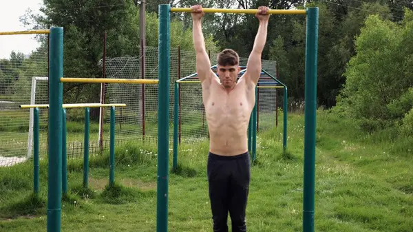 Spor sahasında barfiks çeken kaslı bir sporcu. Genç üstsüz sporcu doğada egzersiz yapıyor. Güçlü sporcu adam dışarıda antrenman yapıyor. Sağlıklı ve aktif yaşam tarzı kavramı. Yavaş çekim