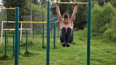 Spor sahasında karın kaslarını çalıştıran güçlü bir adam. Genç sporcu, barfiks çekme çubuğunda egzersiz yapıyor. Doğada spor yapan sporcu. Sportif yaşam tarzı kavramı.