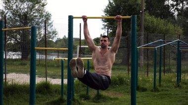 Atletik adam karın kaslarını eğitir spor sahasında yatay barda bacak kaldırır. Genç sporcu, barfiks çekme çubuğunda egzersiz yapıyor. Doğada spor yapan sporcu. Sağlıklı yaşam tarzı.