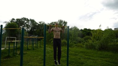 Spor sahasında barfiks çeken kaslı bir sporcu. Genç üstsüz sporcu doğada egzersiz yapıyor. Güçlü sporcu adam dışarıda antrenman yapıyor. Sağlıklı ve aktif yaşam tarzı kavramı. Yavaş çekim