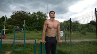 Genç sporcu doğada paralel barlarda şınav çekiyor. Spor alanında egzersiz yapan güçlü bir sporcu. Erkek üstsüz sporcu dışarıda sıkı çalışıyor. Aktif spor yaşam tarzı kavramı. Yavaş çekim