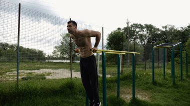Genç sporcu doğada paralel barlarda şınav çekiyor. Spor alanında egzersiz yapan güçlü bir sporcu. Erkek üstsüz sporcu dışarıda sıkı çalışıyor. Aktif spor yaşam tarzı kavramı. Yavaş çekim