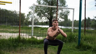 Spor sahasında çömelme hareketleri yapan erkek üstsüz atlet. Yaz doğasında çalışan genç bir sporcu. Güçlü sporcu dışarıda egzersiz yapıyor. Aktif ve sportif yaşam tarzı kavramı. Yavaş çekim
