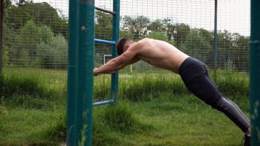 Spor malzemelerinde trisepsler üzerinde egzersiz yapan genç kaslı bir atlet. Spor alanında spor yapan erkek üstsüz bir sporcu. Doğada güçlü bir sporcu eğitimi. Sağlıklı yaşam tarzı kavramı.