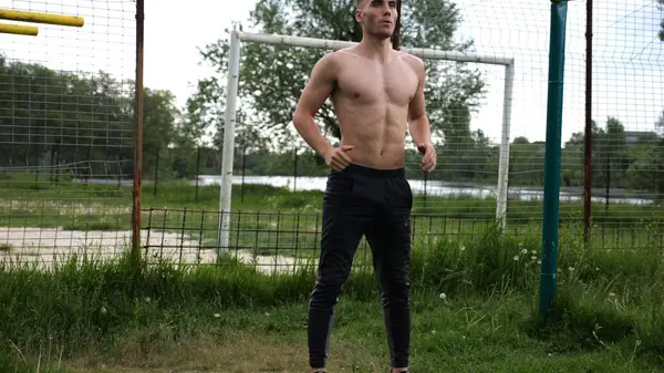 Spor sahasında çömelme hareketleri yapan erkek üstsüz atlet. Yaz doğasında çalışan genç bir sporcu. Güçlü sporcu dışarıda egzersiz yapıyor. Aktif ve sportif yaşam tarzı kavramı. Yavaş çekim