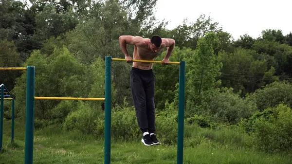 Cesur üstsüz sporcu doğada yatay çıtada şınav çekiyor. Güçlü ve kaslı adam spor alanında antrenman yapıyor. Genç atletik adam dışarıda egzersiz yapıyor. Aktif ve sağlıklı yaşam tarzı kavramı.