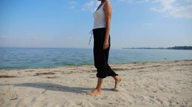 Güneşli bir günde sahilde kumsala giden mutlu yetişkin kadın. Arka planda sakin dalgalarla deniz kıyısında yürüyen güzel bir bayan. Yaz tatili ya da tatil kavramı. Yavaş çekim