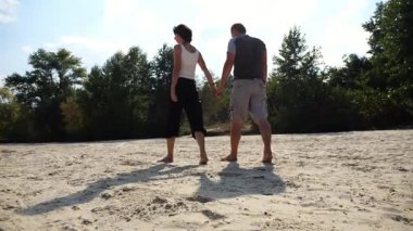 Romantik çift el ele tutuşup kumsalda yürüyor. Güneşli bir günde kıyıya giden mutlu bir çift. Sevgililer tatil köyünde birlikte vakit geçirirler. Yaz tatili veya tatil kavramı