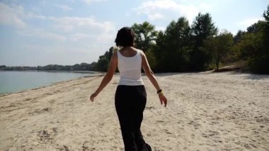 Güneşli bir günde sahilde koşan mutlu yetişkin kadın. Arka planda sakin dalgalarla deniz kıyısında koşan güzel bir bayan. Yaz tatili ya da tatil kavramı. Yavaş çekim