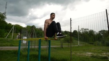 Spor alanında paralel barlarda karın kaslarını çalıştıran güçlü bir adam. Genç üstsüz sporcu doğada egzersiz yapıyor. Doğada spor yapan sporcu. Aktif spor yaşam tarzı kavramı