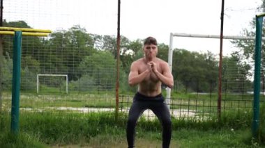 Spor sahasında çömelme hareketleri yapan erkek üstsüz atlet. Yaz doğasında çalışan genç bir sporcu. Güçlü sporcu dışarıda egzersiz yapıyor. Aktif ve sportif yaşam tarzı kavramı. Yavaş çekim