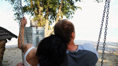 Romantik çift deniz sahilinde salıncakta sallanıyor. Mutlu aşıklar tatil köyünde birlikte vakit geçirmeyi severler. Kaygısız bir çift güneşli bir günde okyanusun kenarında dinleniyor. Yaz tatili veya tatil kavramı.