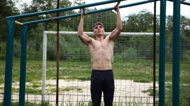 Genç kaslı sporcu spor alanında barfiks çekiyor. Atletik adam dışarıda egzersiz yapıyor. Yaz doğasında spor yapan güçlü bir adam. Sağlıklı ve aktif yaşam tarzı kavramı. Yavaş çekim