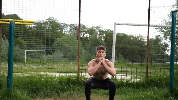 Spor sahasında çömelme hareketleri yapan erkek üstsüz atlet. Yaz doğasında çalışan genç bir sporcu. Güçlü sporcu dışarıda egzersiz yapıyor. Aktif ve sportif yaşam tarzı kavramı. Yavaş çekim