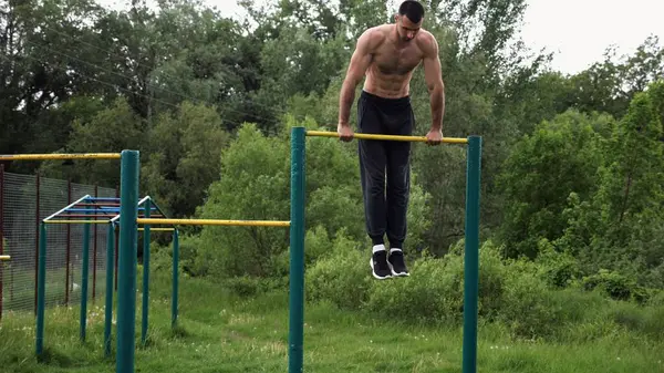 Cesur üstsüz sporcu doğada yatay çıtada şınav çekiyor. Güçlü ve kaslı adam spor alanında antrenman yapıyor. Genç atletik adam dışarıda egzersiz yapıyor. Aktif ve sağlıklı yaşam tarzı kavramı.