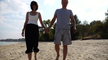 Güneşli bir günde deniz kıyısına giden mutlu bir çift. Romantik çift el ele tutuşup sahilde yürüyor. Sevgililer tatil köyünde birlikte vakit geçirirler. Yaz tatili ya da tatil kavramı. Yavaş çekim