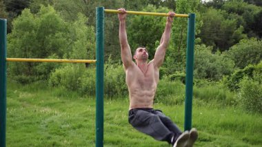 Atletik adam karın kaslarını eğitir spor sahasında yatay barda bacak kaldırır. Genç sporcu, barfiks çekme çubuğunda egzersiz yapıyor. Doğada spor yapan sporcu. Sağlıklı yaşam tarzı.