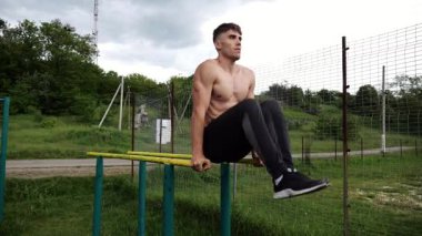Spor alanında paralel barlarda karın kaslarını çalıştıran güçlü bir adam. Genç üstsüz sporcu doğada egzersiz yapıyor. Doğada spor yapan sporcu. Aktif spor yaşam tarzı kavramı.