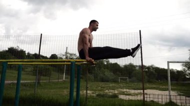 Güçlü bir adam karın kaslarını eğitir spor sahasında paralel barlarda bacak kaldırır. Genç üstsüz sporcu doğada egzersiz yapıyor. Doğada spor yapan sporcu. Sportif yaşam tarzı kavramı.