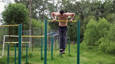Cesur üstsüz sporcu doğada yatay çıtada şınav çekiyor. Güçlü ve kaslı adam spor alanında antrenman yapıyor. Genç atletik adam dışarıda egzersiz yapıyor. Aktif ve sağlıklı yaşam tarzı kavramı.